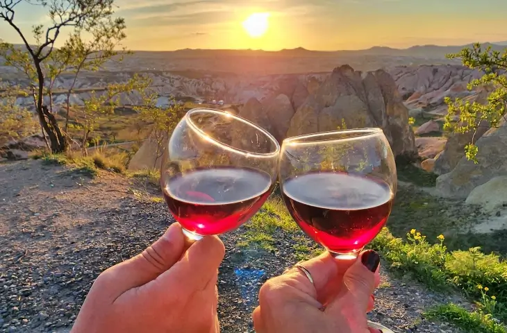 Kapadokya Kızılçukur Vadisi’nde gün batımında manzaraya karşı tutulan iki kadeh şarap